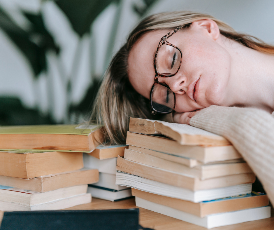 Kobieta śpiąca z głową na książkach - czuje się wyczerpana.