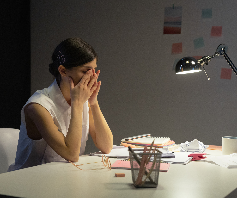 Pracoholizm - kobieta zmęczona pracą siedzi przy biurku.